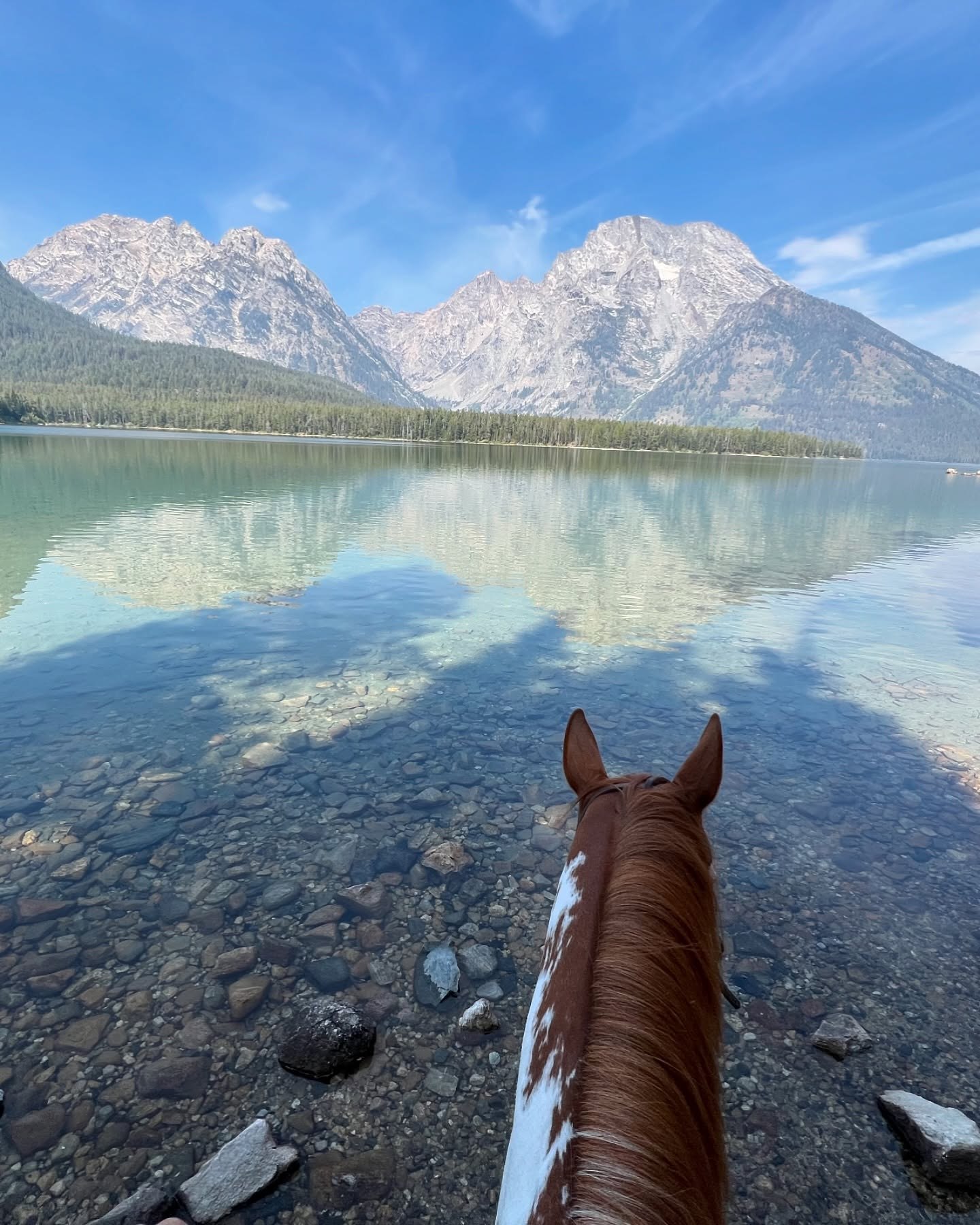 View from horseback beside a glassy mountain lake reflecting dramatic peaks