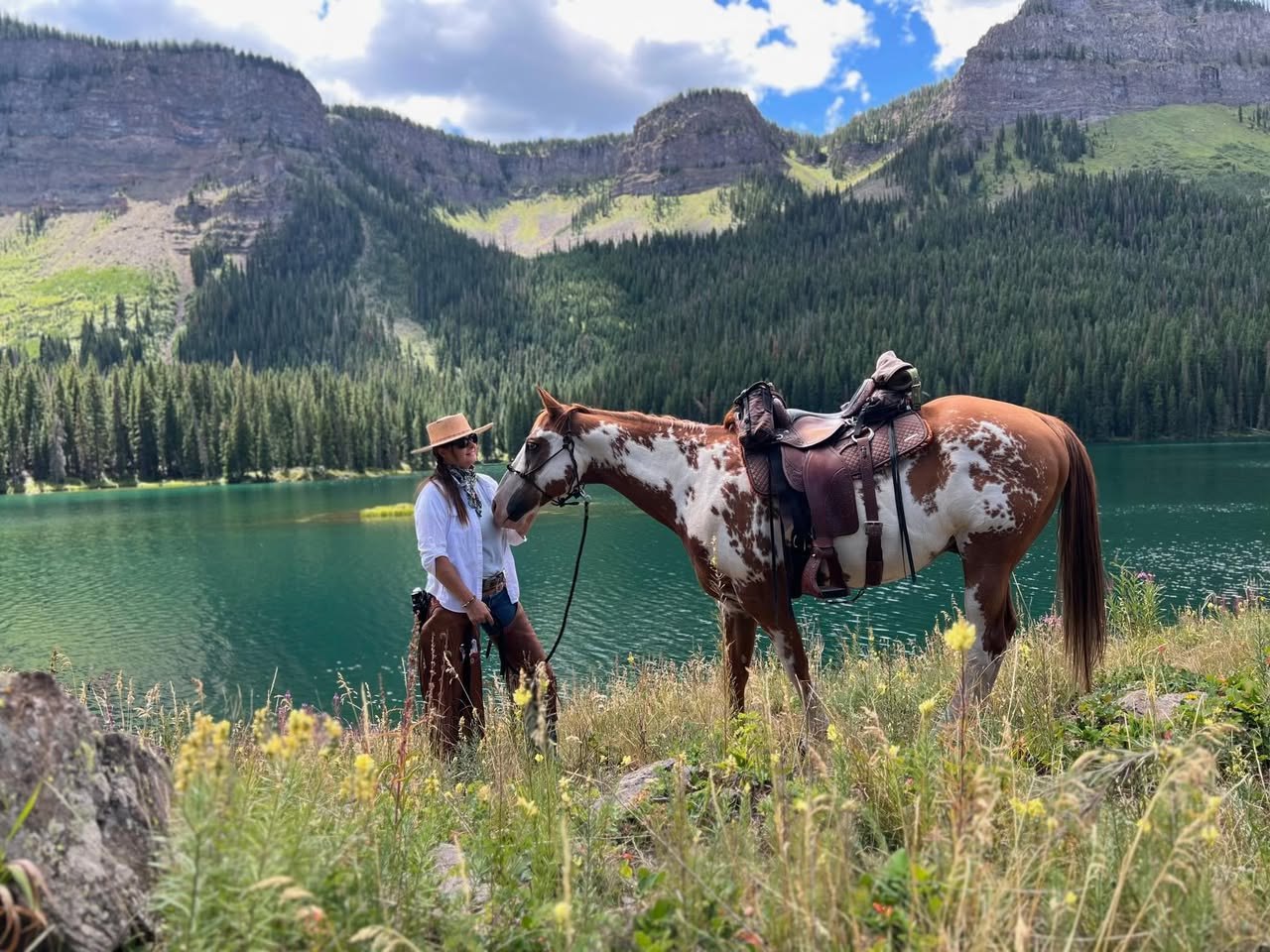 Bree beside her paint horse overlooking a turquoise alpine lake and mountain basin